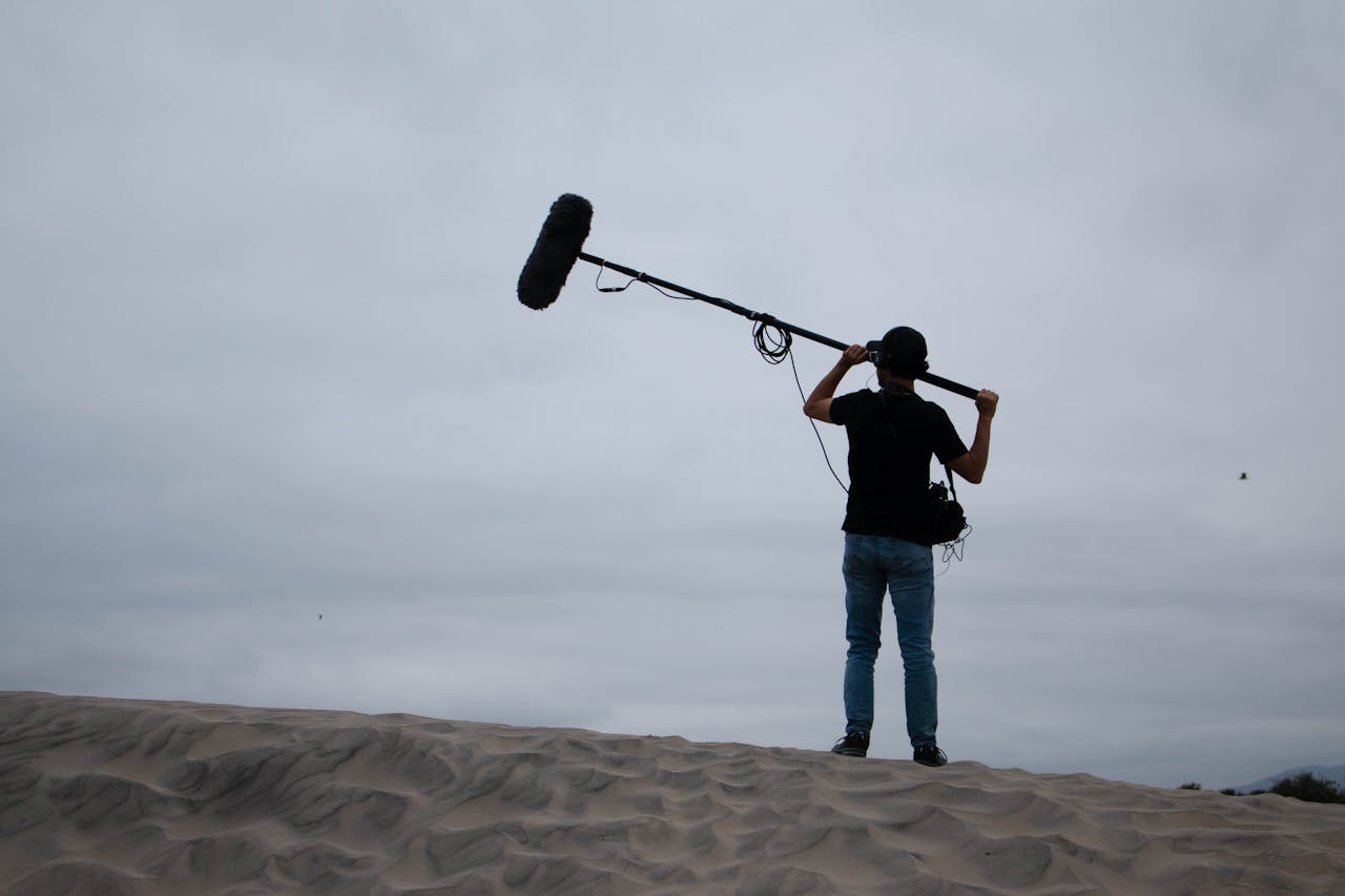 Back view of sound technician with boom mic on sandy dunes, working outdoors.